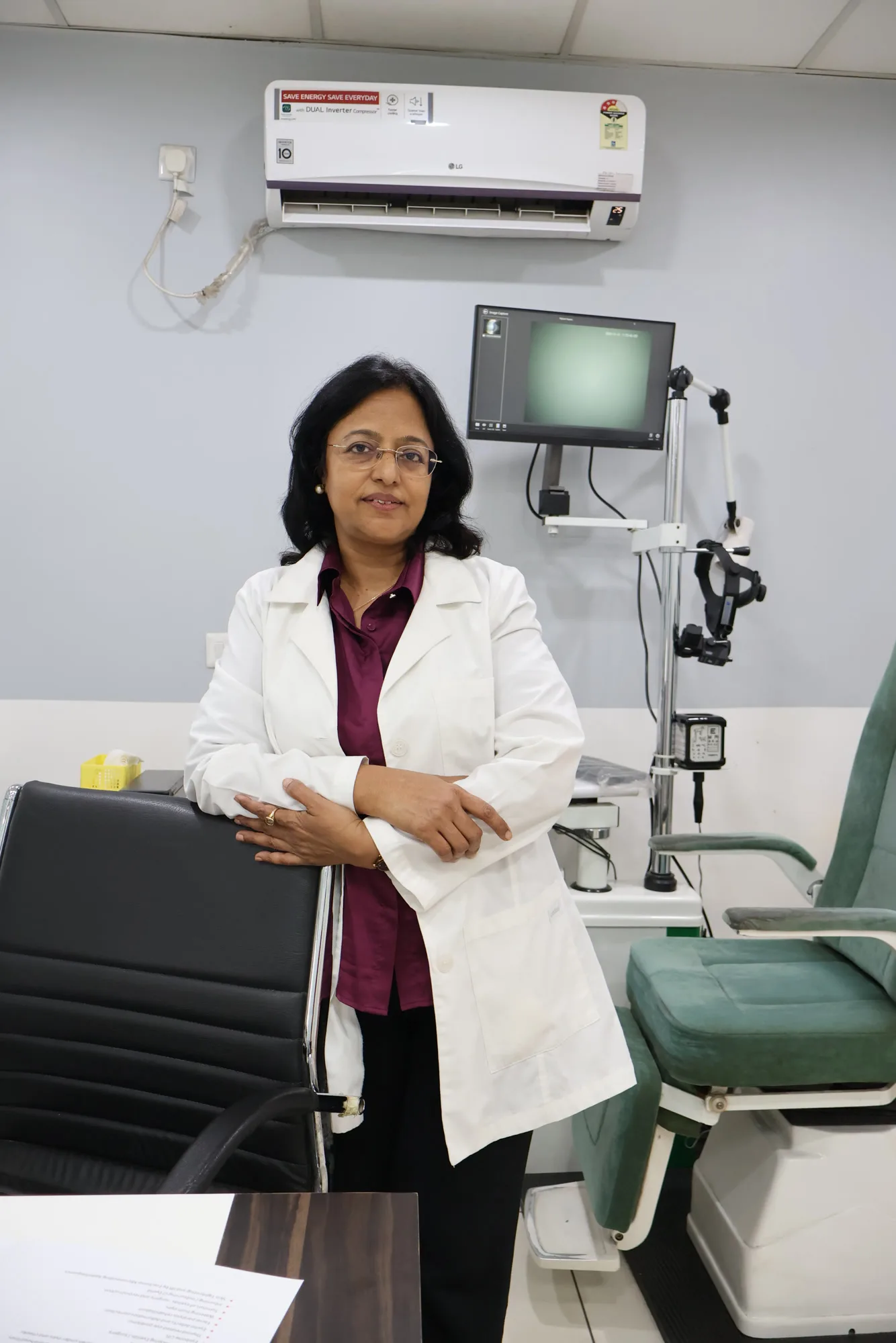 Dr. Poonam Jain in a white coat, standing beside a chair in a consultation room