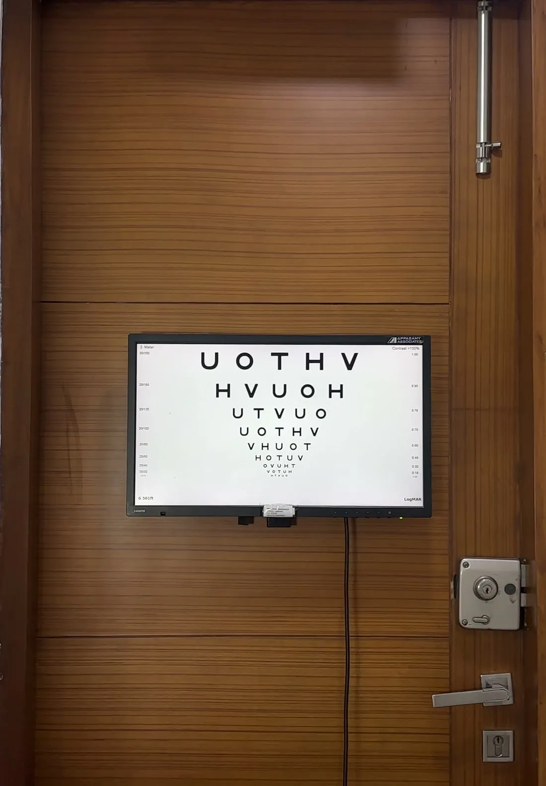 A wooden examination-room door with an eye-chart screen beside it