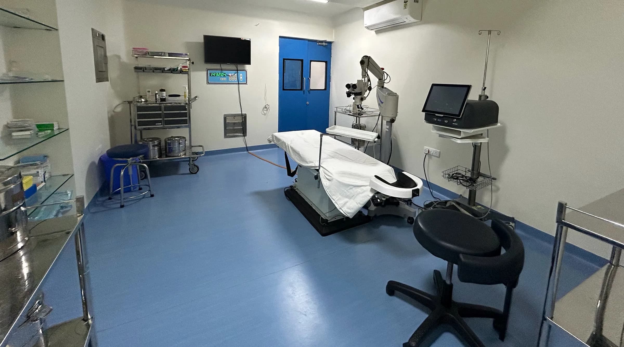 An operation theatre from a corner, with shelving, a trolley, the operating table and the microscope