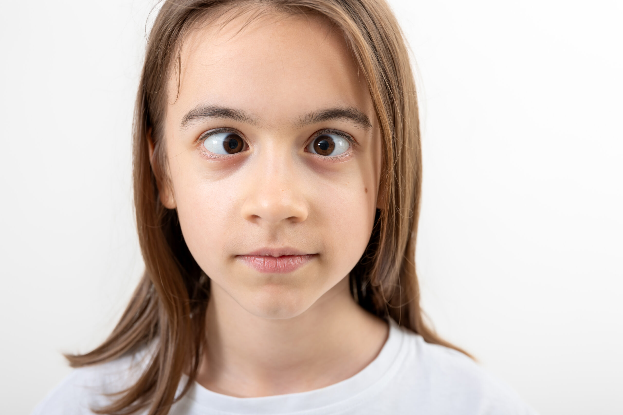 Caucasian teenage girl in a white T-shirt grimaces on a white background isolated.