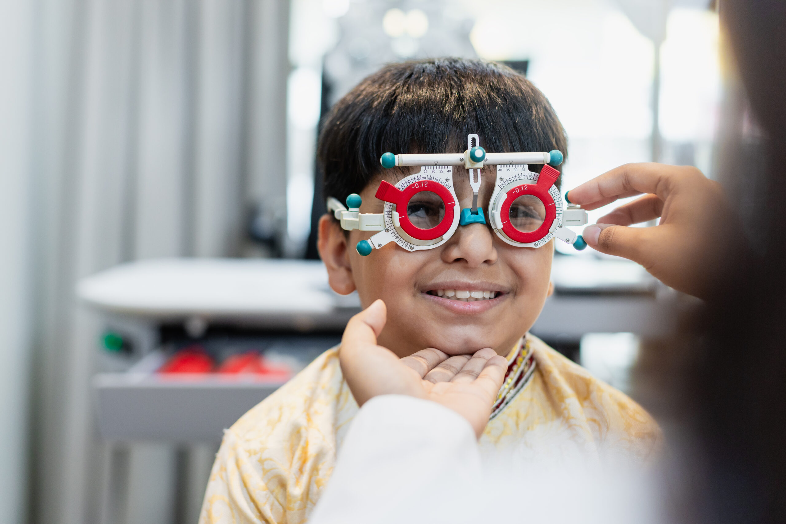 Happy Indian child boy with women eye specialist examining eyesight modern ophthalmology equipment in clinic. Patient kid male checkup iris examines ophthalmological hospital. measure eyeglasses.