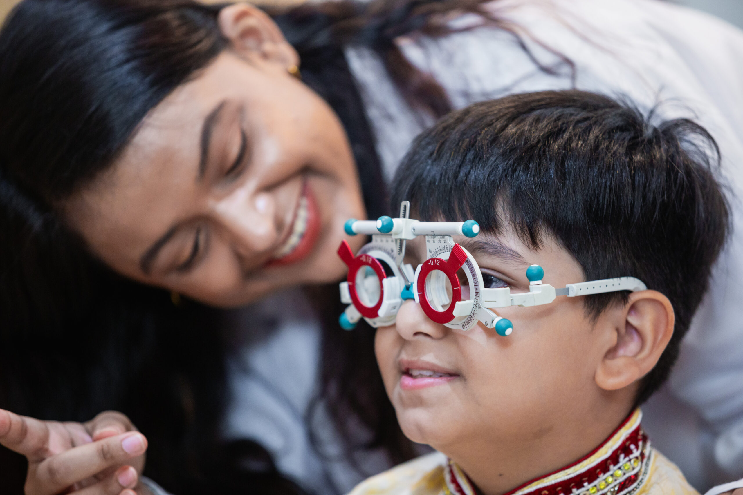 Happy Indian child boy with women eye specialist examining eyesight modern ophthalmology equipment in clinic. Patient kid male checkup iris examines ophthalmological hospital. measure eyeglasses.
