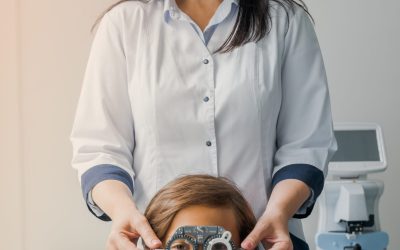 Cheerful middle aged ophthalmologist examining little boy with modern equipment. Female optician helping small patient select googles, eye vision sight frame lenses