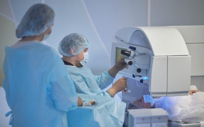 middle aged man operating surgical microscope while performing procedure on woman lying on operating table, woman assisting nearby