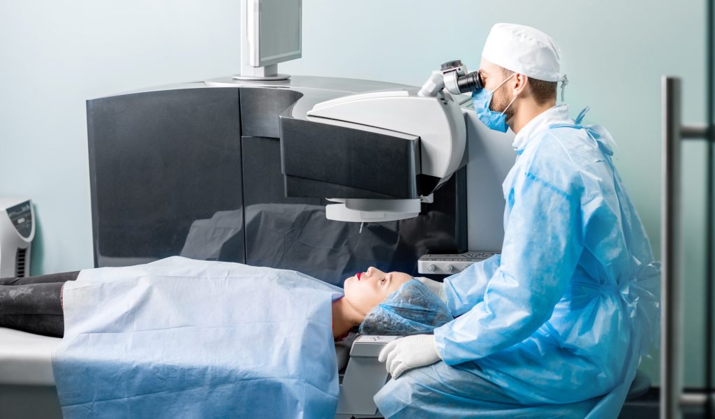 Eye surgeon operating woman with laser vision correction machine in the operating room