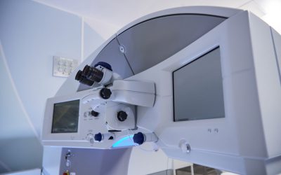 Medical operating room showing advanced surgical microscope and digital display monitors positioned for precision procedures, emphasizing modern healthcare technology equipment